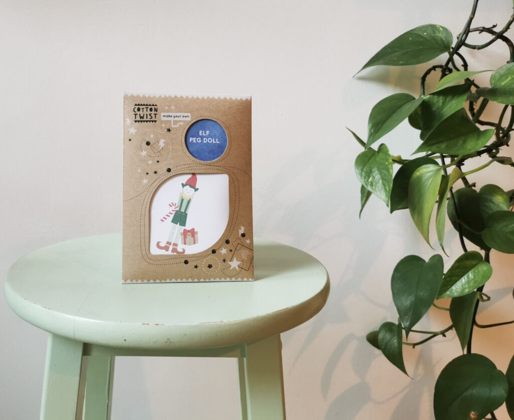 Elf peg doll on a green stool with a green plant to the right