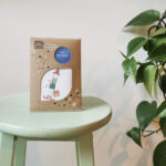 Elf peg doll on a green stool with a green plant to the right