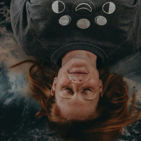 A woman lies on her back on a yoga mat with eyes closed and a peaceful expression